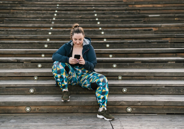 Junge Frau in Sportklamotten sitzt auf Treppen mit ihrem Handy