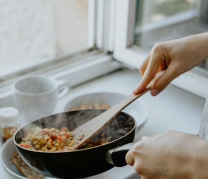 Eine Pfanne mit gekochten Gemüse wird über einen Teller gehalten, um das Essen darauf zu tun.