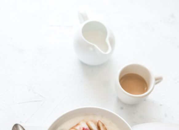 Eine Joghurt Bowl mit Früchten steht zusammen mit einem Buch und einer Tasse Kaffee auf einer weißen Platte