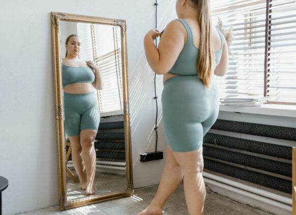 Übergewichtige Frau schaut sich im Spiegel an