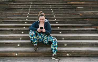 Junge Frau in Sportklamotten sitzt auf Treppen mit ihrem Handy