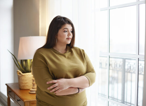 Junge Frau mit Übergewicht am Fenster