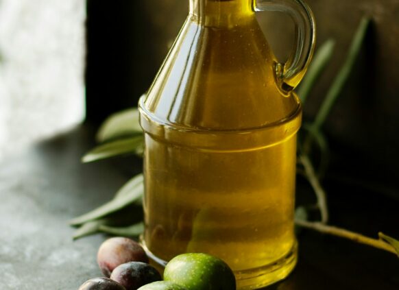 Glasflasche mit Olivenöl und Oliven davor