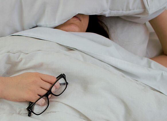 Frau liegt erschöpft im Bett mit Brille in der Hand