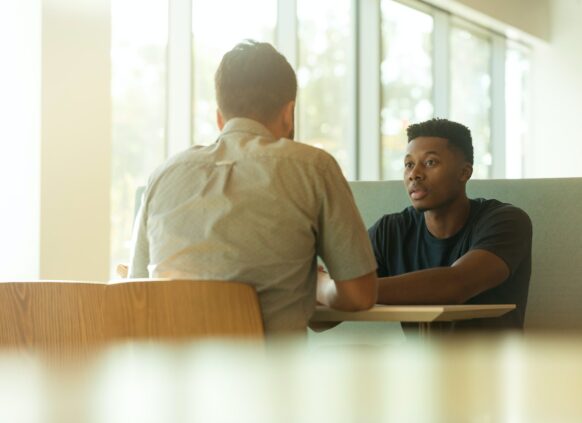 Zwei junge Männer sitzen sich gegenüber und sprechen miteinander