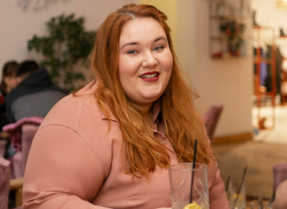 Laxhende übergewichtige Frau hält ein Glas in der Hand.