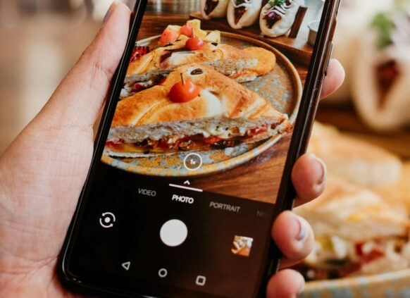 Zu sehen ist eine hand, die ein Smartphone hält, auf dessen Display gerade ein Gericht fotographiert wird-