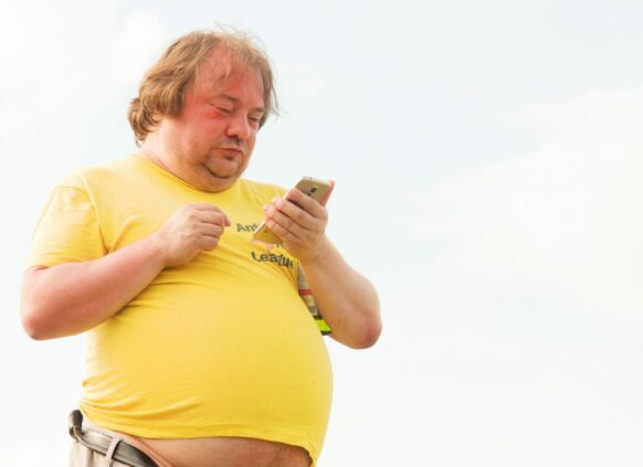 Übergewichtiger Mann im gelben T-Shirt schaut auf sein Smartphone