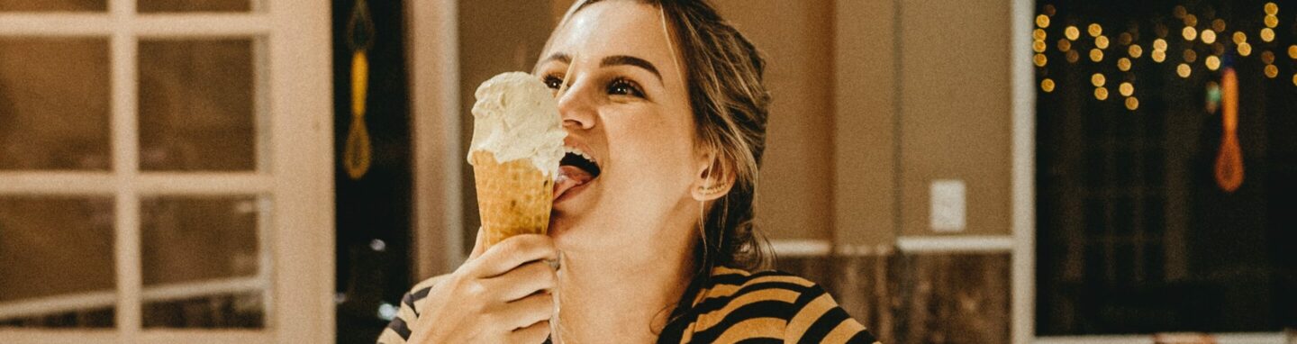 Frau steht vor einer Theke im geringelten Shirt und isst glücklich ein Eis