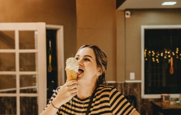 Frau steht vor einer Theke im geringelten Shirt und isst glücklich ein Eis