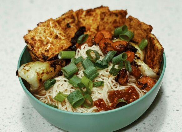 Bowl mit Tofu, Nudeln, Gemüse und Frühlingszwieblen auf einer Küchenplatte