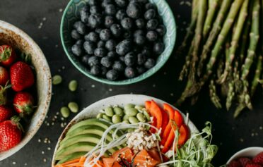 Bowl mit Avocado, Lachs und weiterem Gemüse auf einer dunklen Platte mit Obst