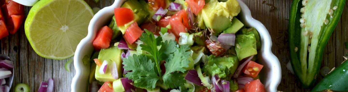 Teller mit buntem Salat auf einer Holzplatte umgeben von verschiedenen Gemüse Sorten