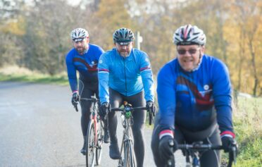 Drei Herren mittleren Alters fahren gemeinsam föhlich Rennrad in der Natur
