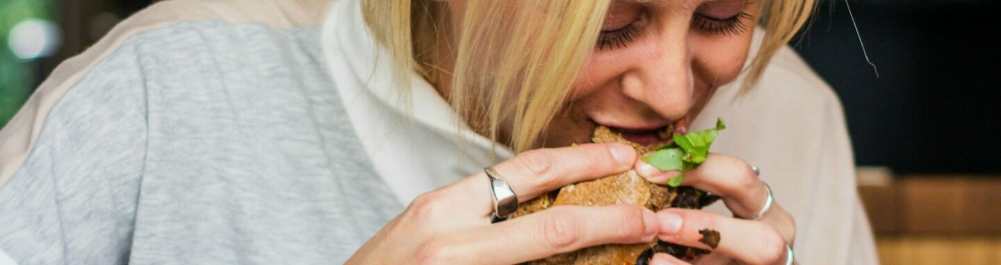 Frau isst einen Burger und vor ihr auf dem Tisch iegt noch mehr Junkfood.