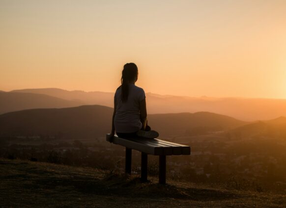 Frau sitzt im Sonnenuntergang auf einer Bank auf einem Berg.