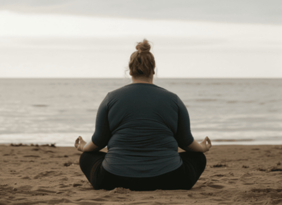 PLus size Frau meditiert am Strand.