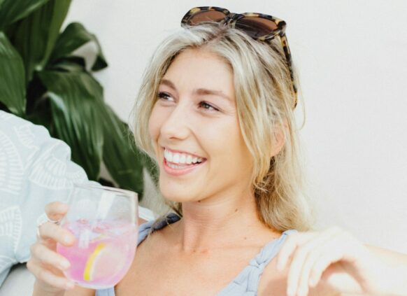 Eine junge lachende Frau hält ein Glas Limonade in der Hand.