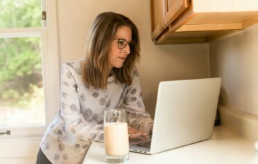 Eine Frau steht an ihrem Laptop, neben ihr steht ein Glas Milch.