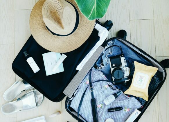 Ein gepackter Koffer ist aufgeklappt auf dem Boden. Darin befinden sich klassiche Strandurlaubssachen, wie ein Sonnenhut und Kleidung.