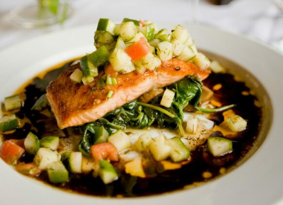 Lachs mit Gemüse und Soße auf einem Teller garniert.
