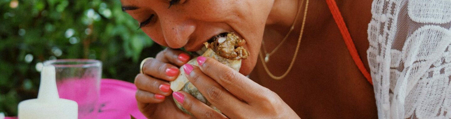 Eine asiatische Frau isst einen Burrito und sieht sehr glücklich dabei aus.