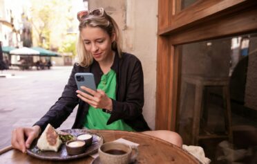 Eine junge blonde Frai sitzt im Restaurant und trackt auf ihrem Smartphone Kalorien