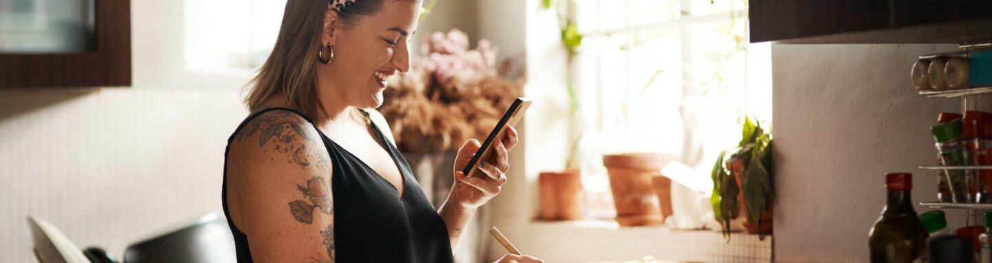 Woman looking at a recipe app on her phone and cooking