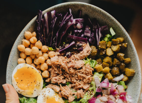 Person holding healthy salad bowl with tuna and egg